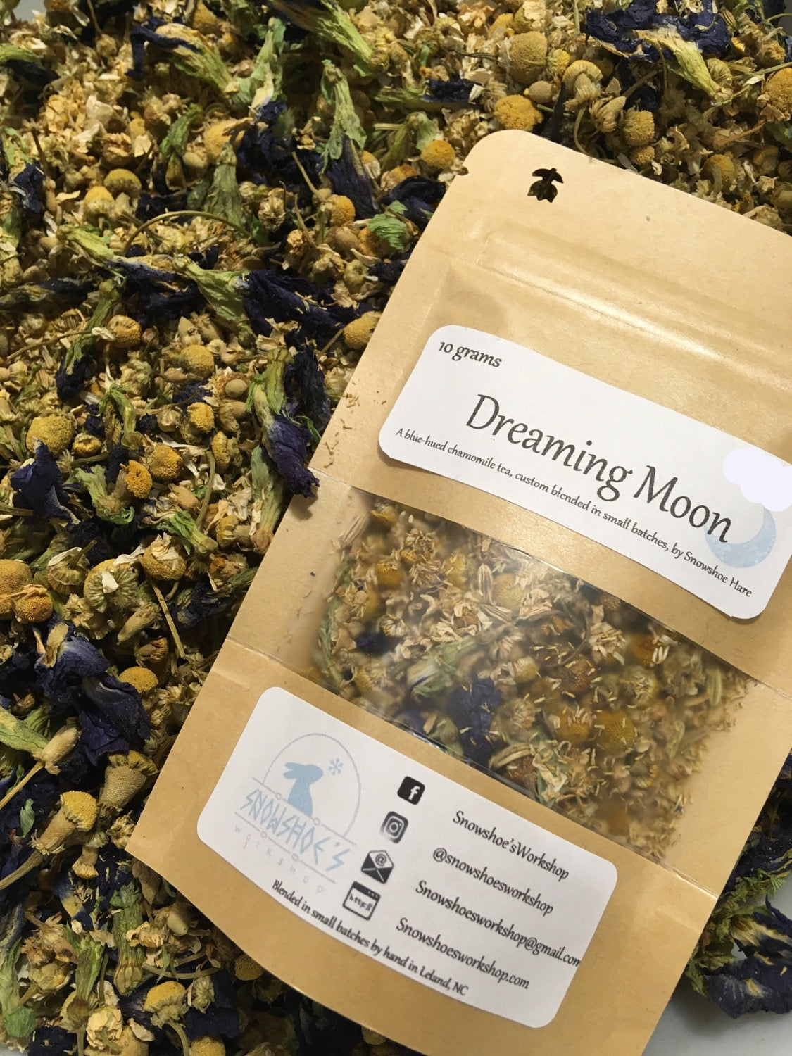 Tea packaging labeled 'Dreaming Moon' surrounded by dried herbs and flowers.