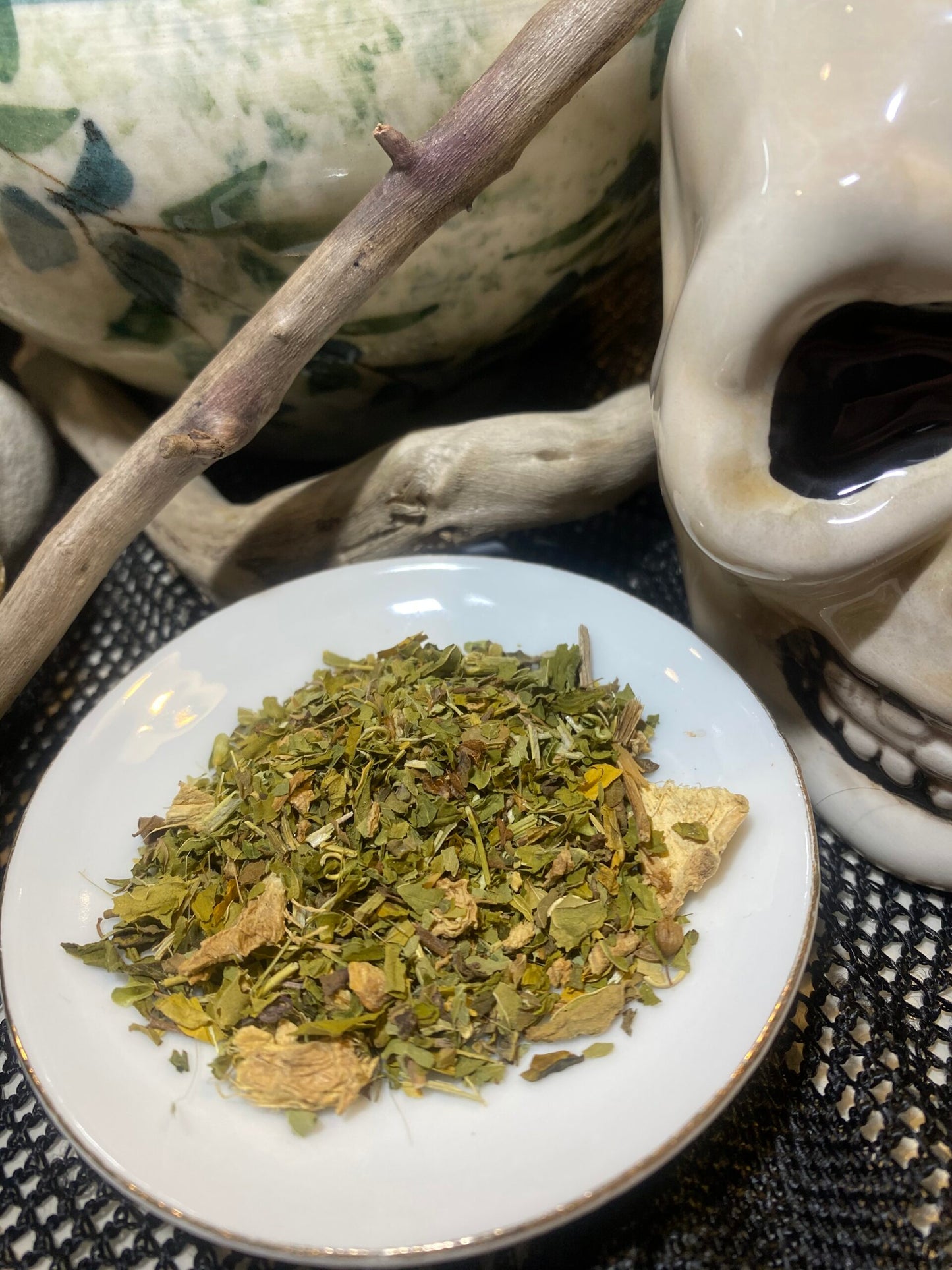 Dried herbs on a white plate with a skull-shaped container in the background