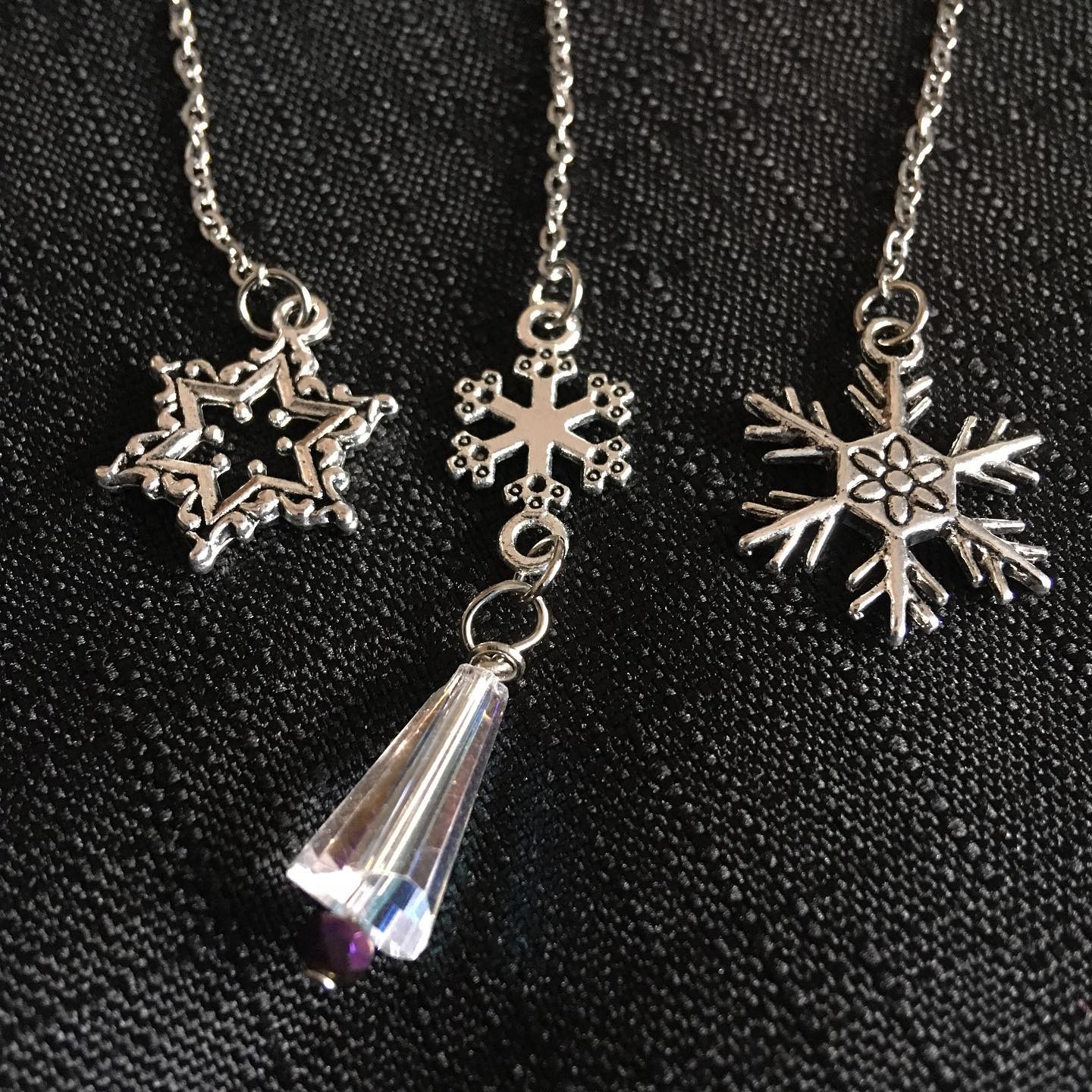 Three silver snowflake charms on a chain on a black background