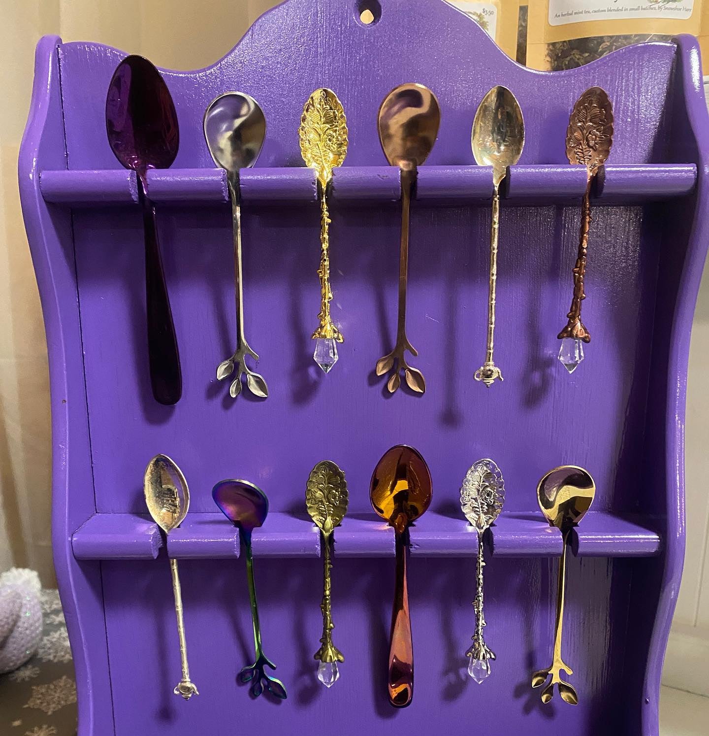 Purple wall-mounted shelf with various decorative spoons on a plain background