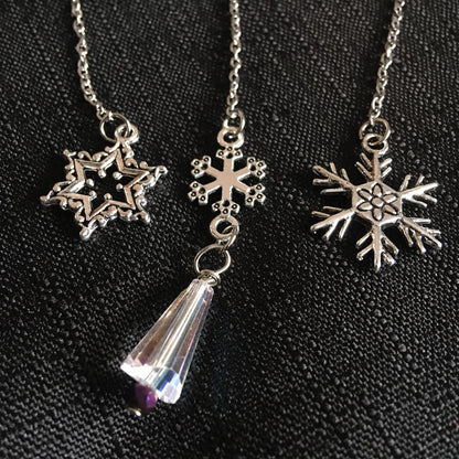 Three silver snowflake charms on a chain on a black background