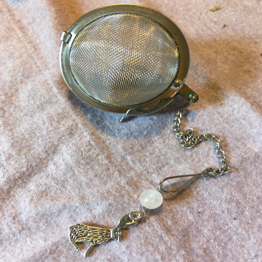 Tea ball with chain and decorative charm on a textured surface